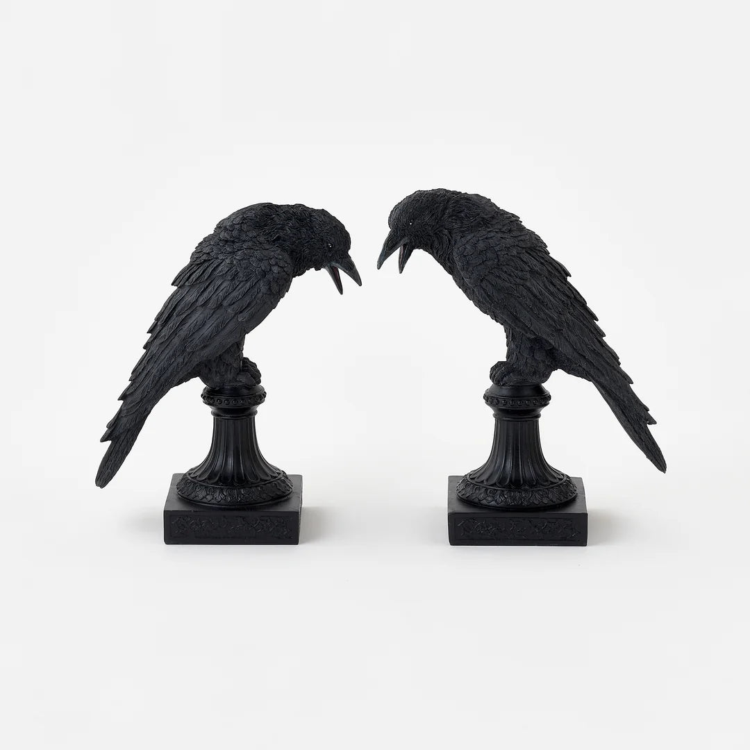 2 black crow figurines perched on decorative pedestals with square bases, shown against a plain light background.