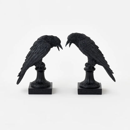 2 black crow figurines perched on decorative pedestals with square bases, shown against a plain light background.