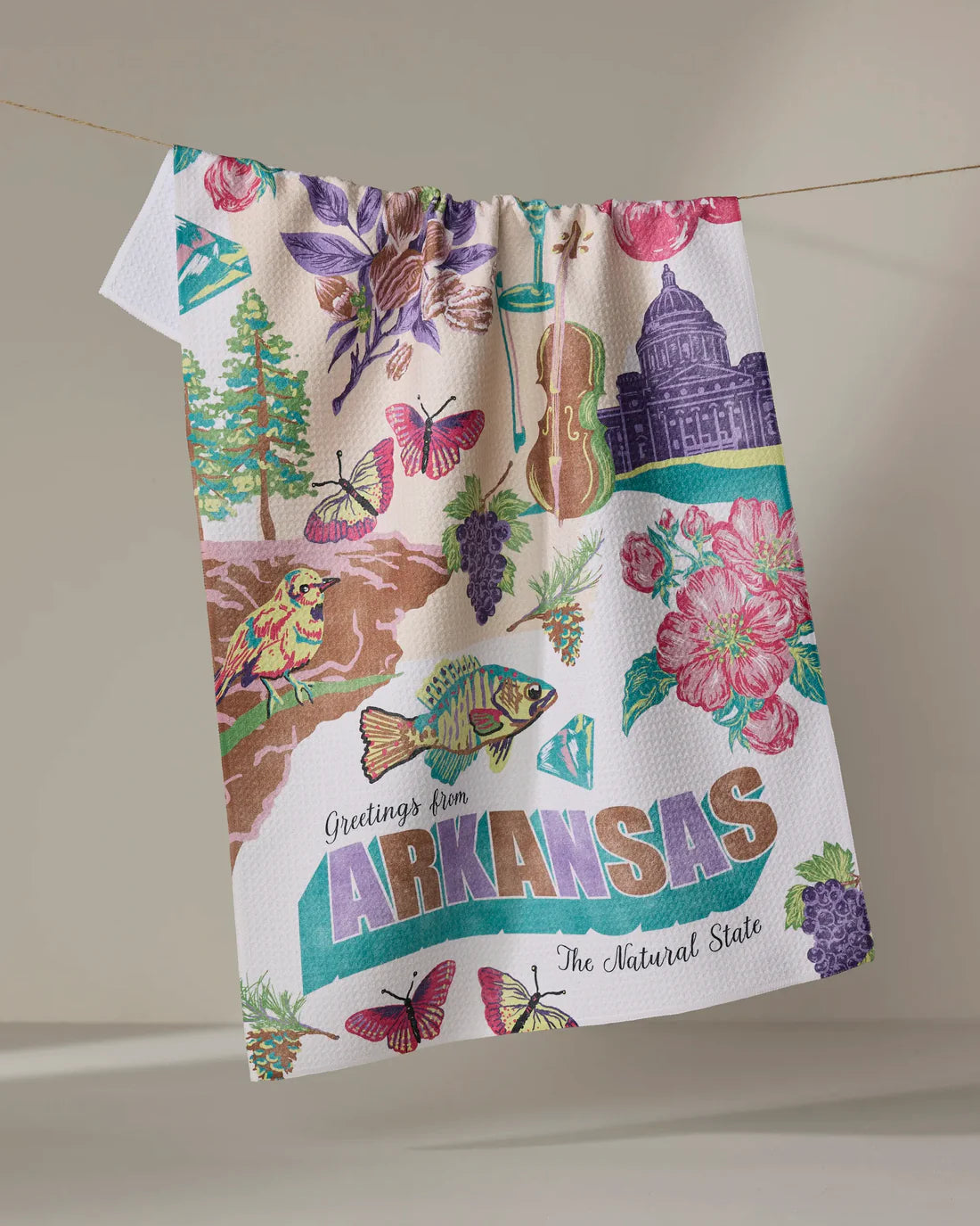 Greetings From Arkansas Tea Towel hanging on a line on a beige background