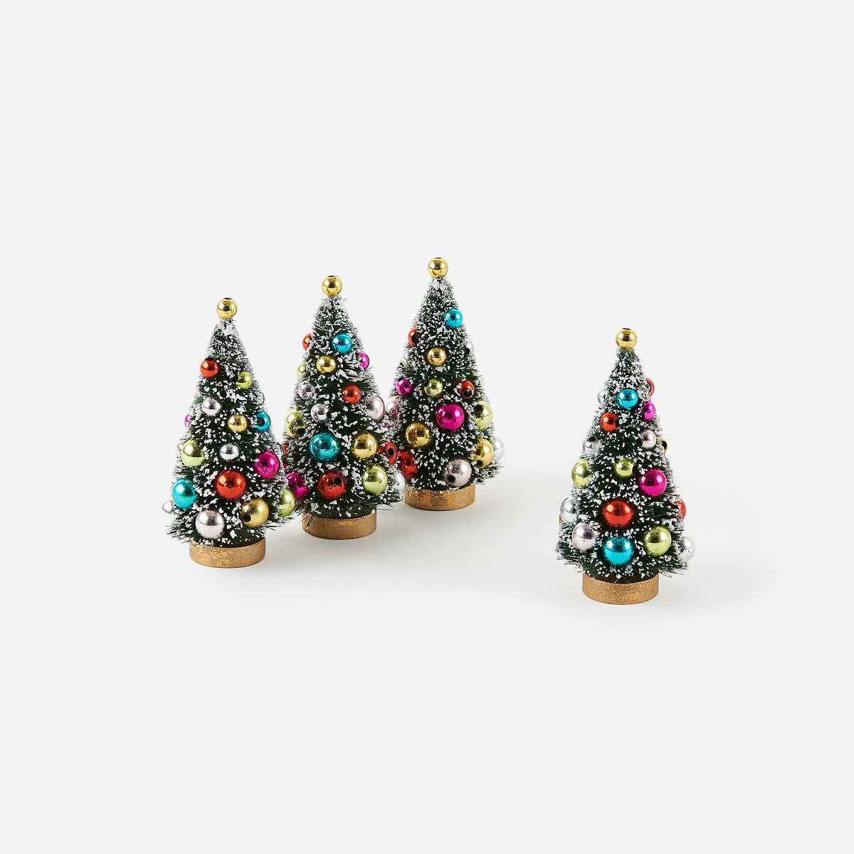 4 snow flecked bottle brush trees with ornaments on them