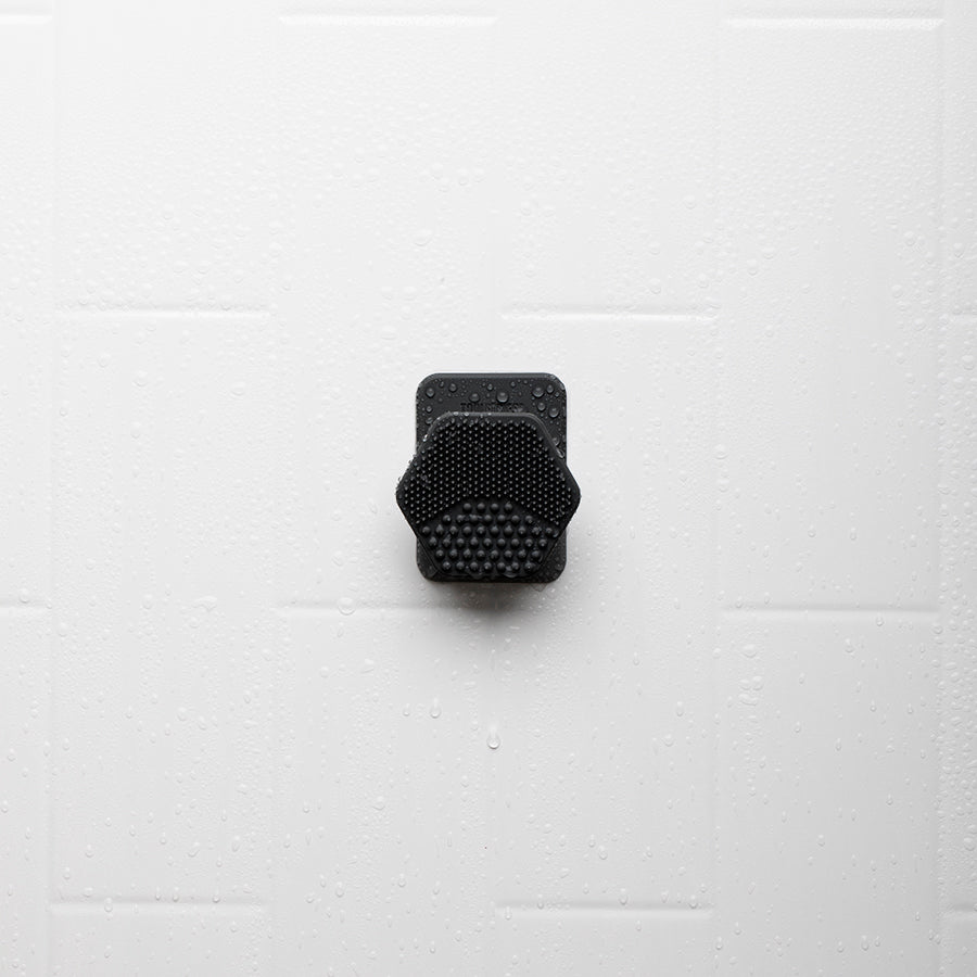scrubber in holder hanging on a white tile shower.