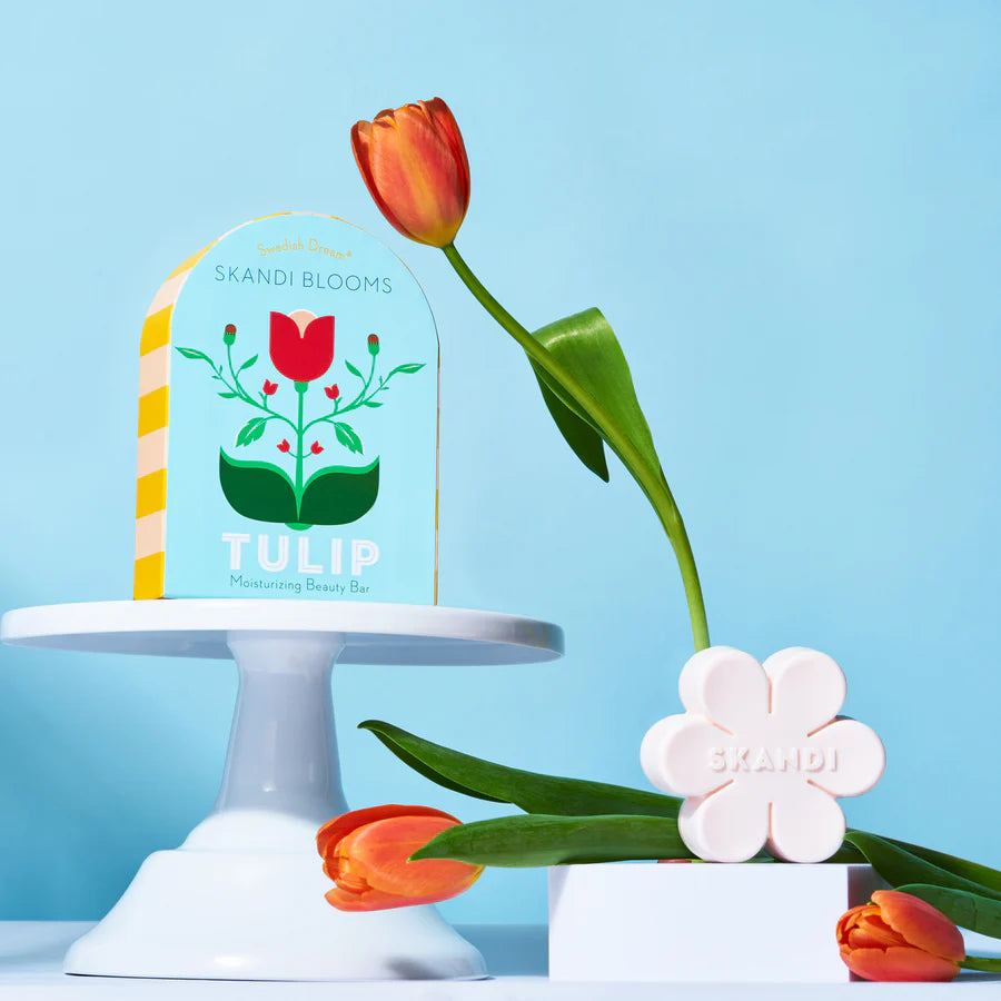 blue box with floral design is set on a cake riser, with tulips arranged around it.