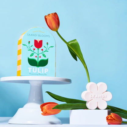 blue box with floral design is set on a cake riser, with tulips arranged around it.