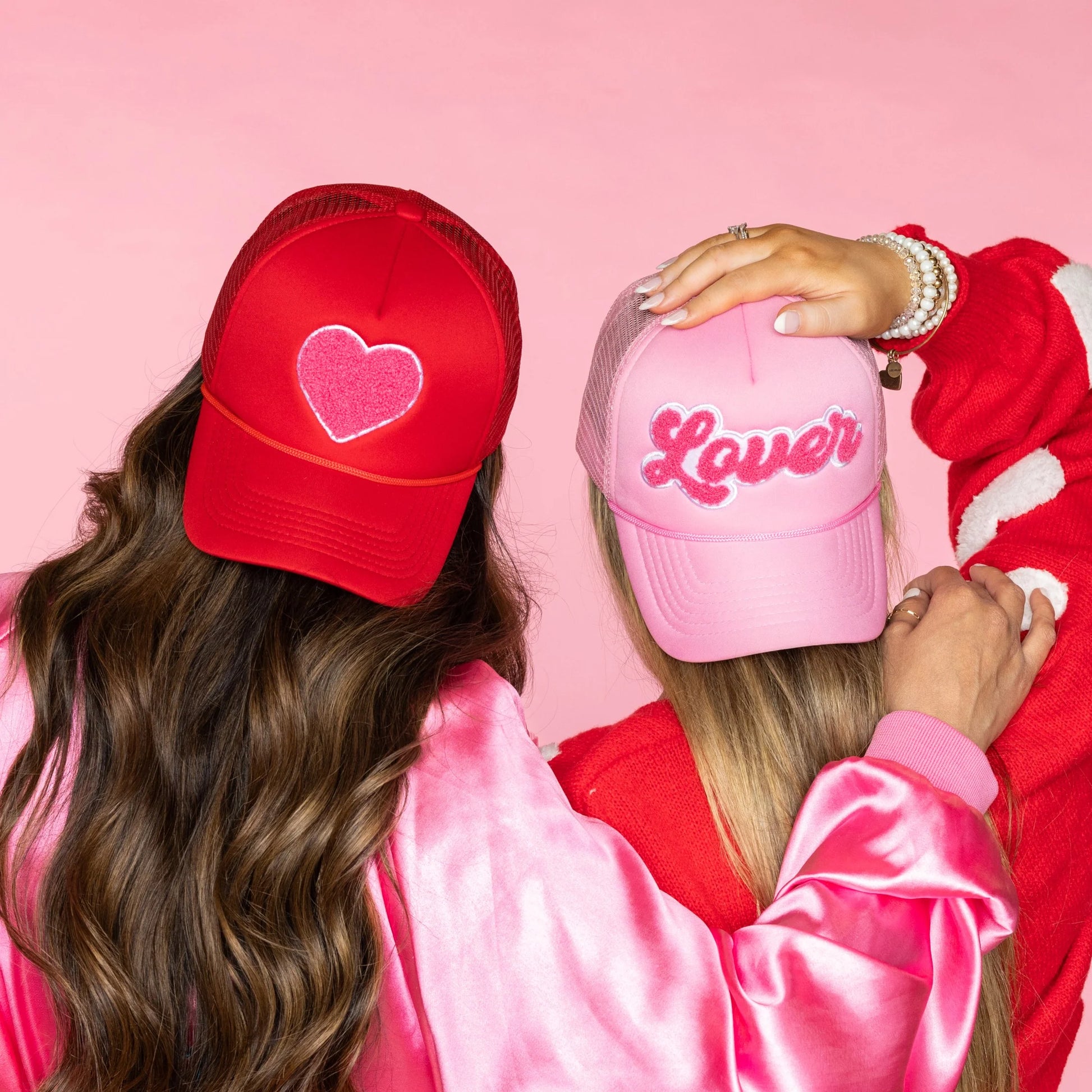 2 people wearing trucker hats, one is red with heart on it, the other is pink with "lover on it.