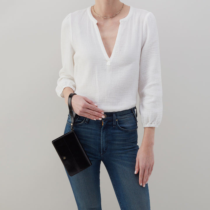 person wearing jeans and a white blouse with black jill wristlet on their arm.