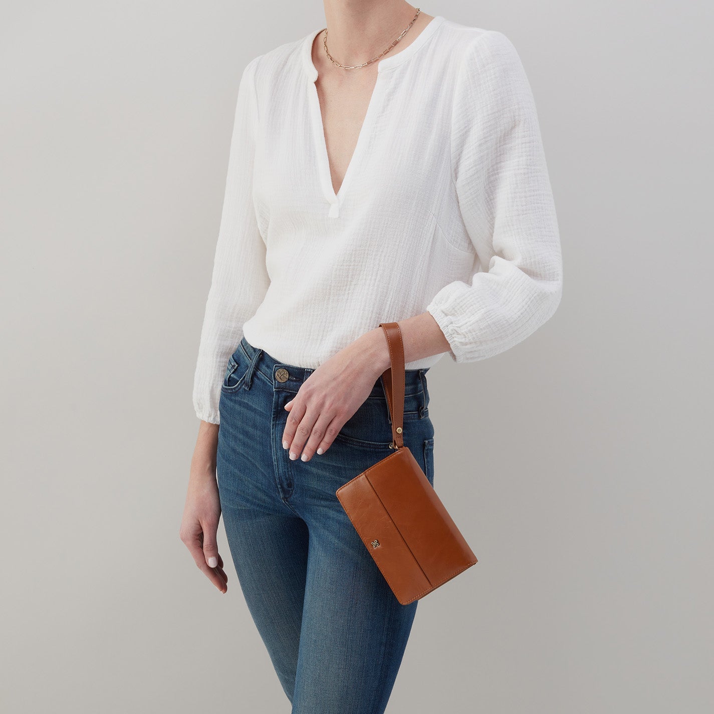 person wearing jeans and a white blouse with truffle jill wristlet on their arm.