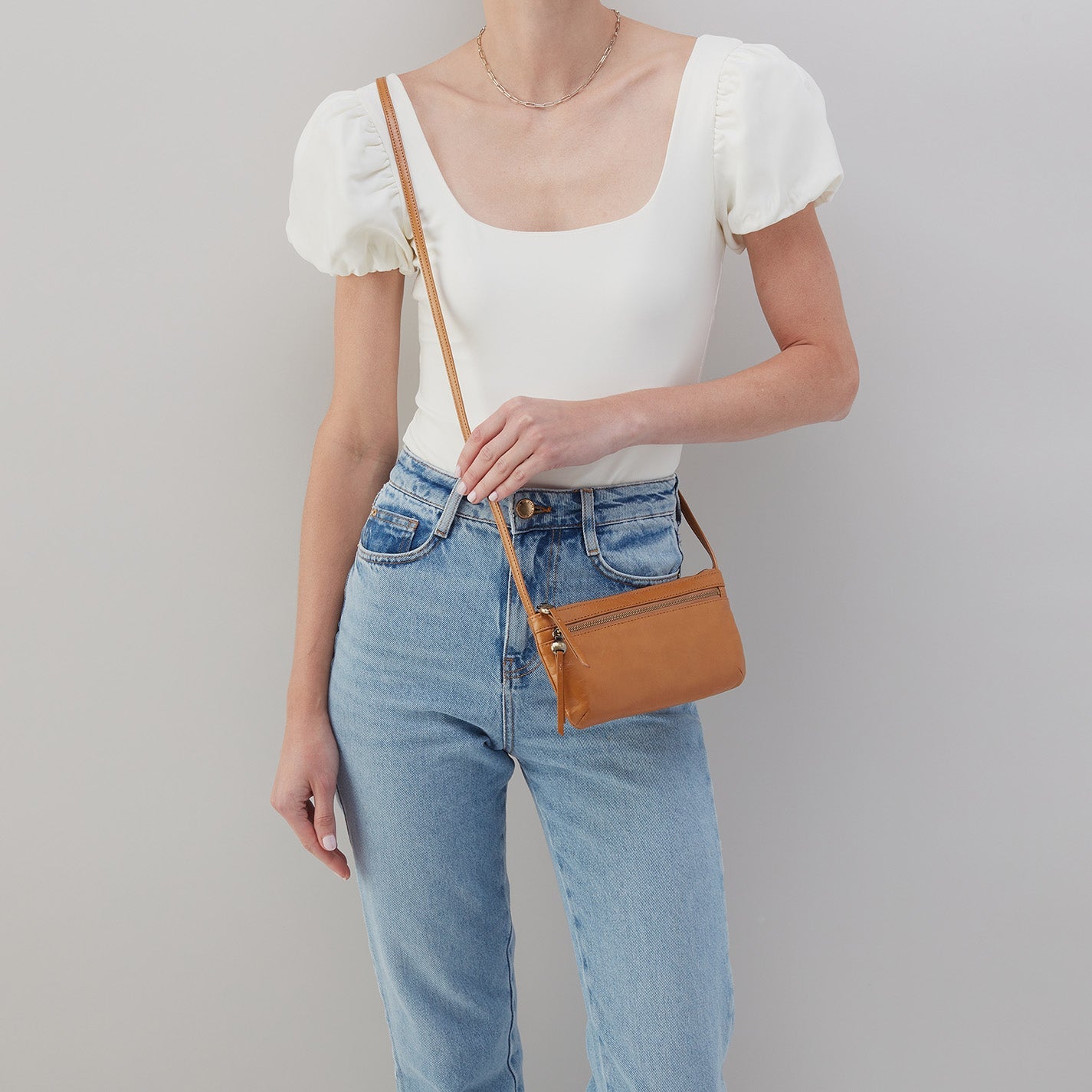 person wearing jeans and a white top with the natural cara crossbody over their shoulder.
