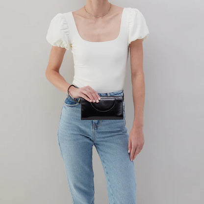 person wearing jeans and a white top holding black zenith wristlet in front of themself.