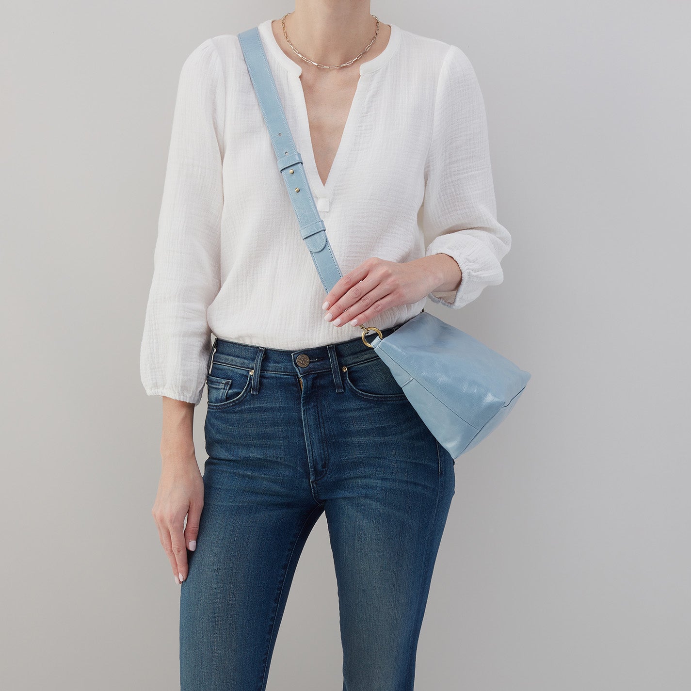 person wearing jeans and a white top with cornflower Ashe Crossbody on their shoulder.