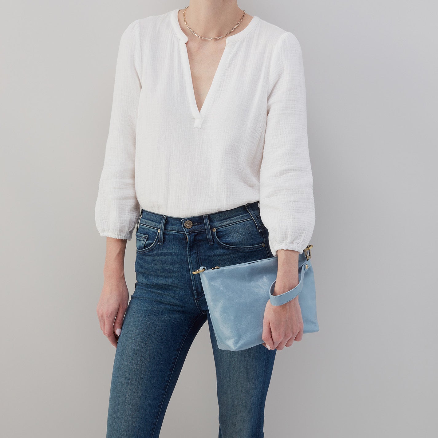 person wearing jeans and a white top holding cornflower Ashe Crossbody as a clutch.