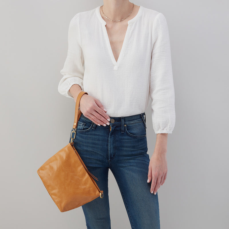 person wearing jeans and a white top with Ashe Crossbody hanging on their wrist with the wristlet strap.