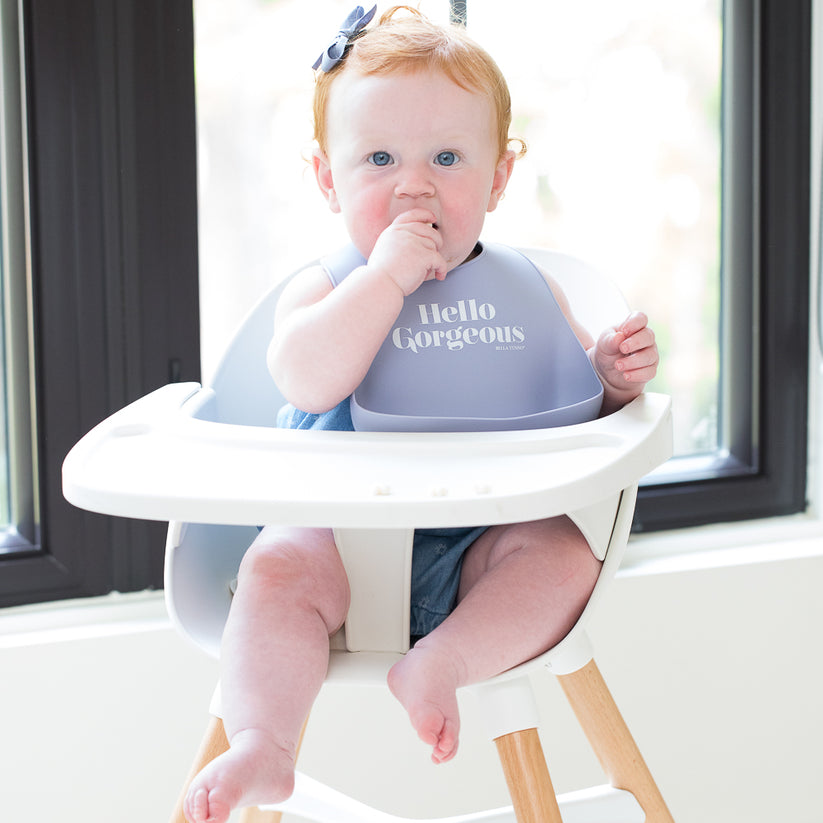 baby sitting in highchair wearing "hello gorgeous" bib.