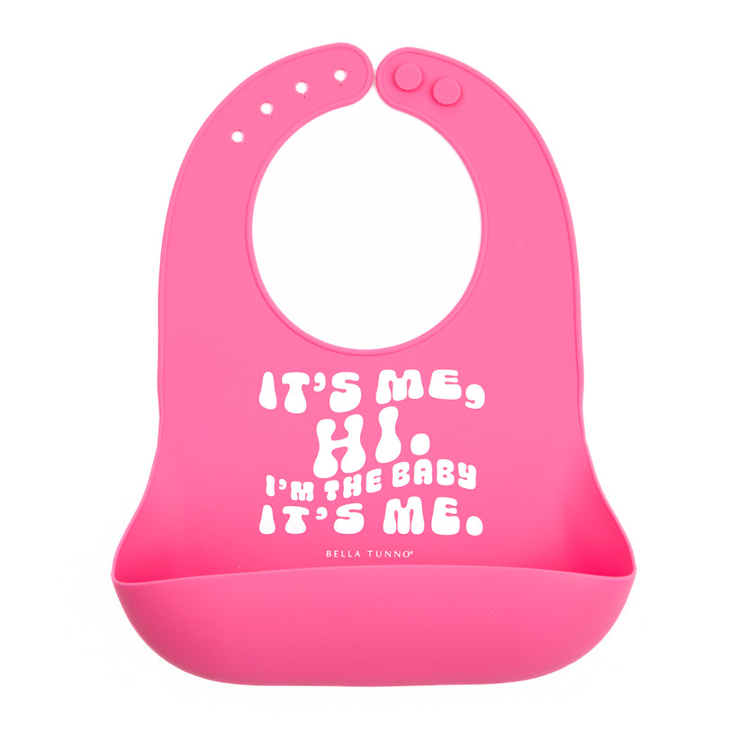 pink silicone bib printed with "it's me, hi. i'm the baby it's me" in white.