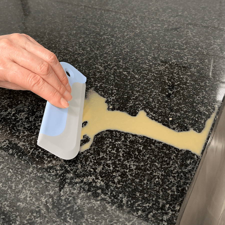 Person using a mini squeegee to remove a spilled liquid from a black surface
