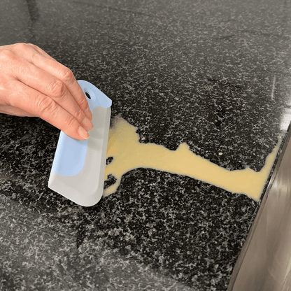 Person using a mini squeegee to remove a spilled liquid from a black surface