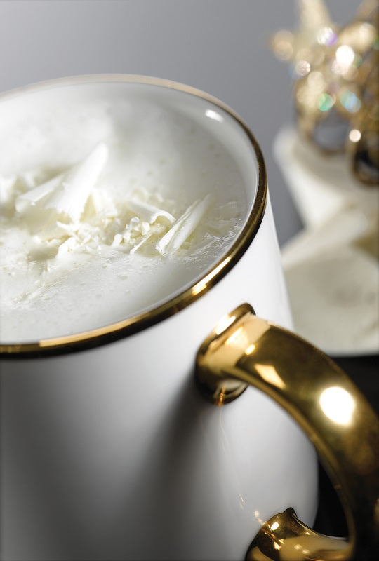 close up of white mug with gold handle and rim filled with white hot chocolate.