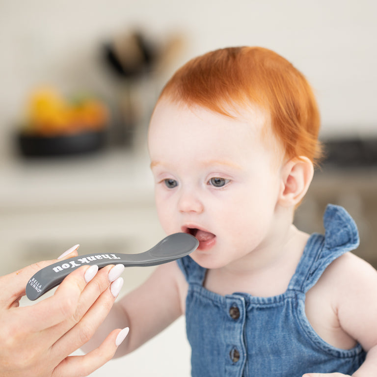 a little girl being fed by her mother with the thank you spoon