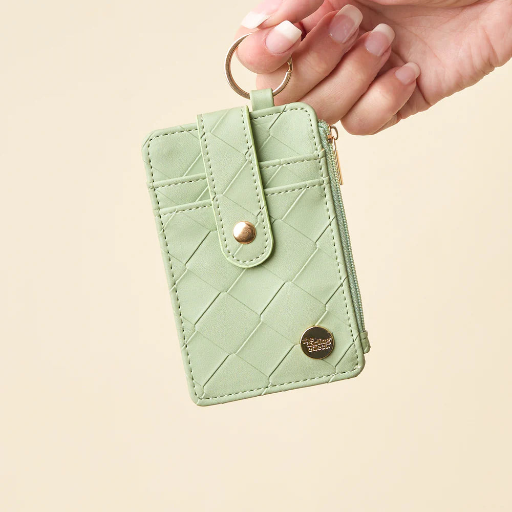 person holding sage Woven Keychain Wallet with their finger through the gold ring key chain on a light beige background
