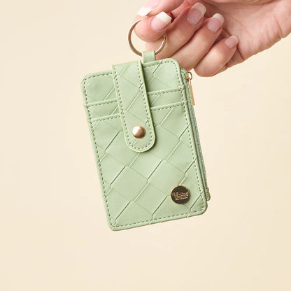 person holding sage Woven Keychain Wallet with their finger through the gold ring key chain on a light beige background