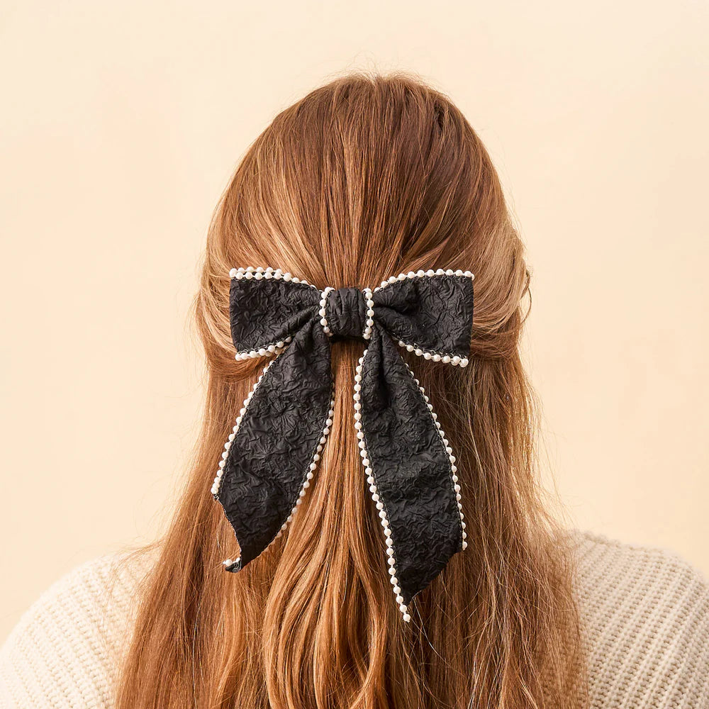 back view of persons with light brown hair partially clipped up with a black pearl bow.