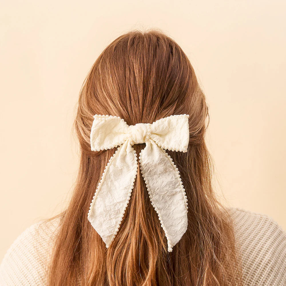 back view of person with light brown hair partially clipped up with cream pearl bow.