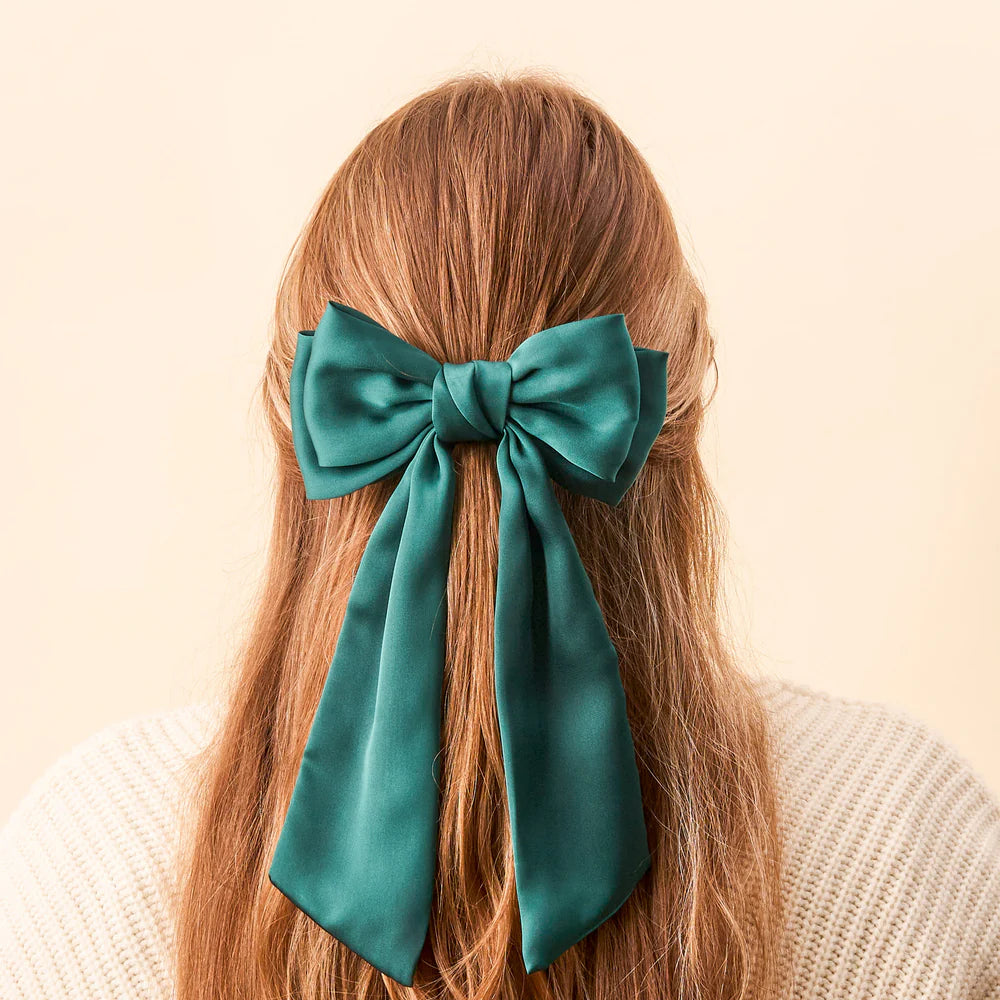 person with light brown hair partially pulled up with a green satin bow clip.