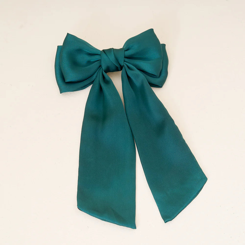 green satin bow clip laying on an off-white background.