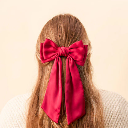 person with light brown hair partially clipped up with a red satin hair bow.