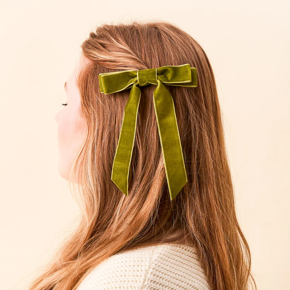 person with light brown hair with a green velvet bow clipped in it.