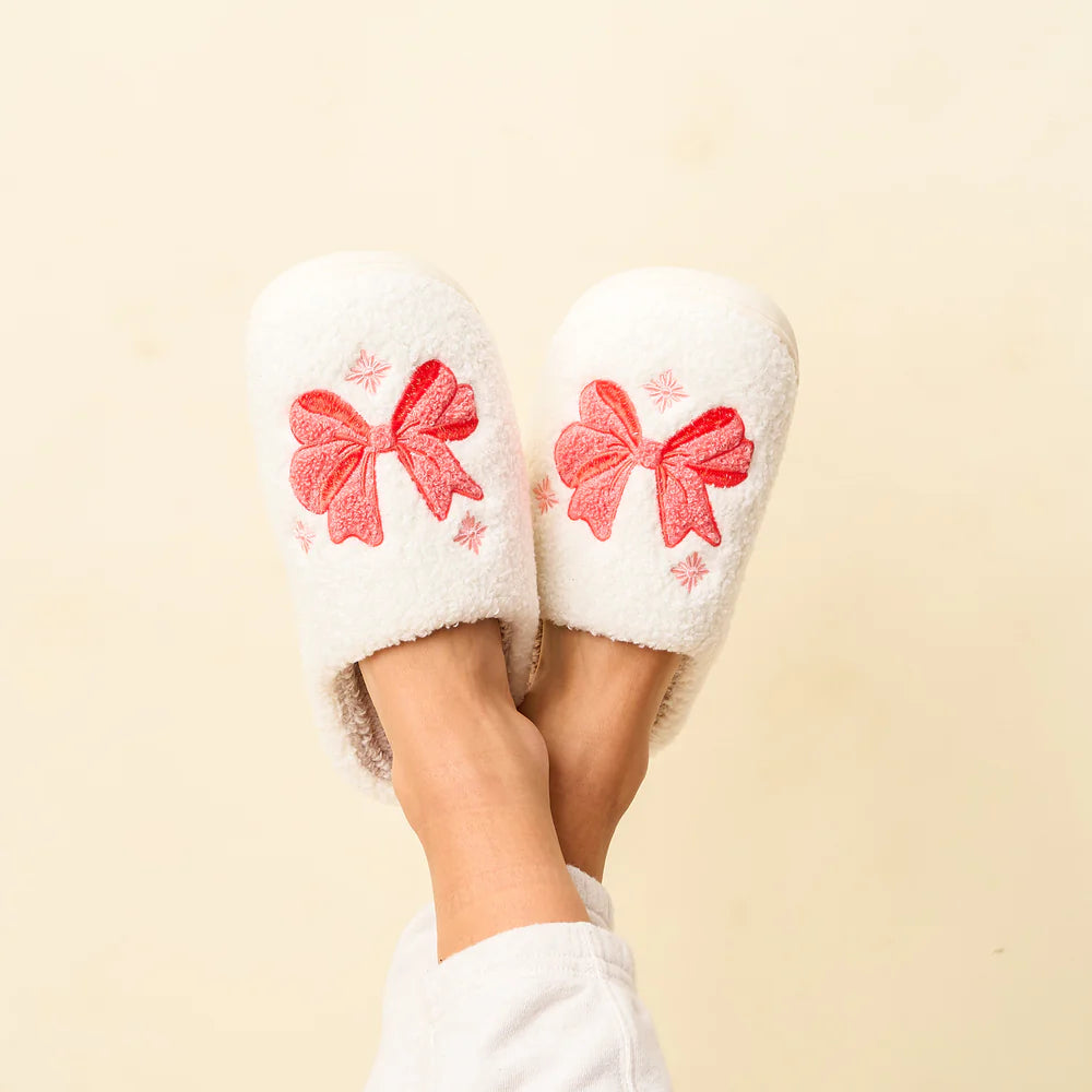 feet crossed in the air wearing white fuzzy slippers with pink bows on the.