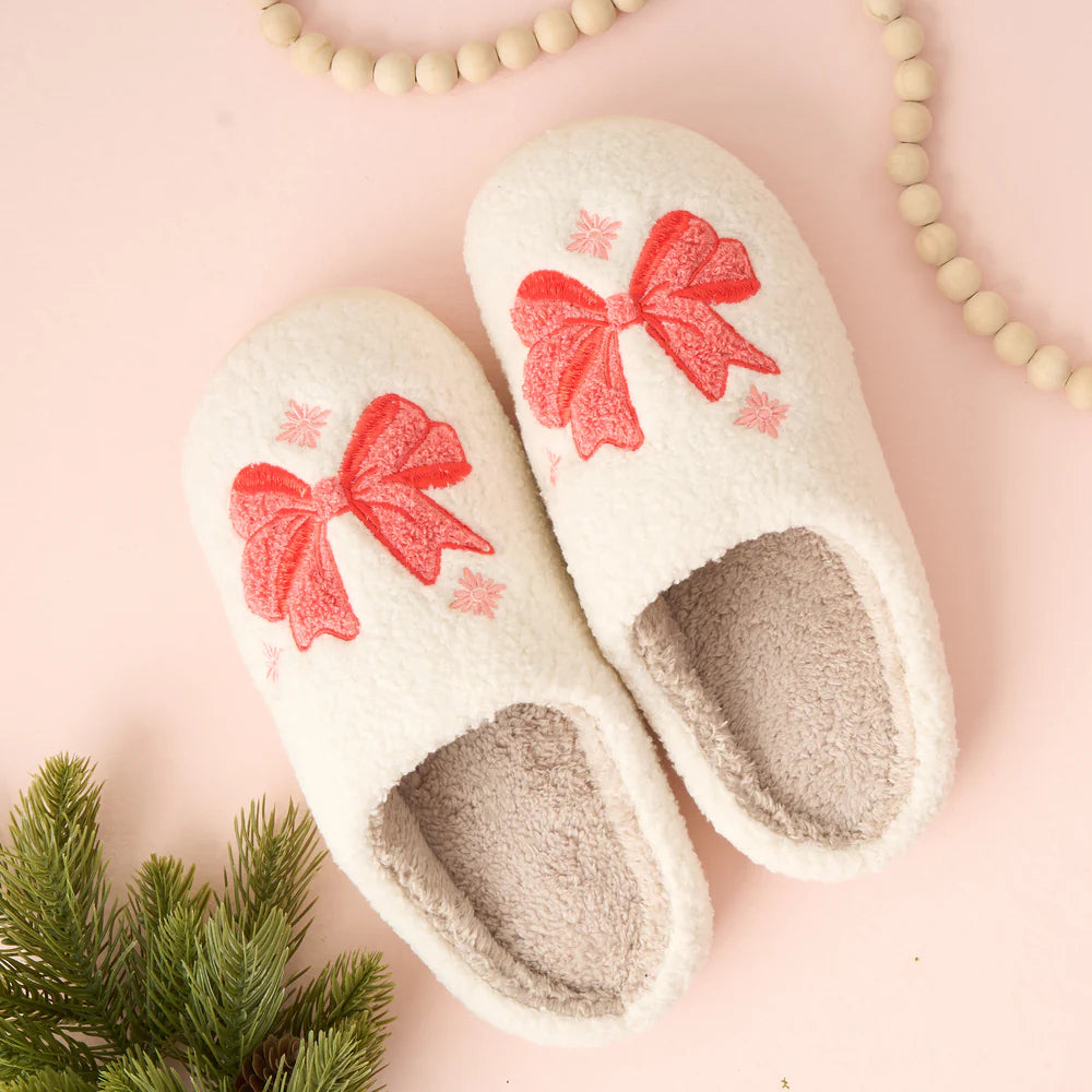 bow slippers set on a light pink background with a string of beads and a sprig of greenery.