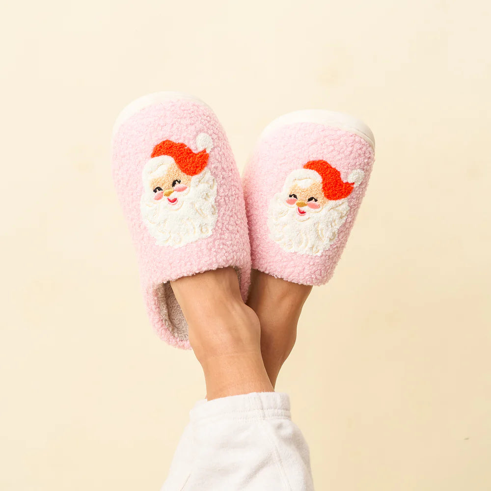 feet crossed in the air wearing pink fuzzy slippers with a Santa face on each one.