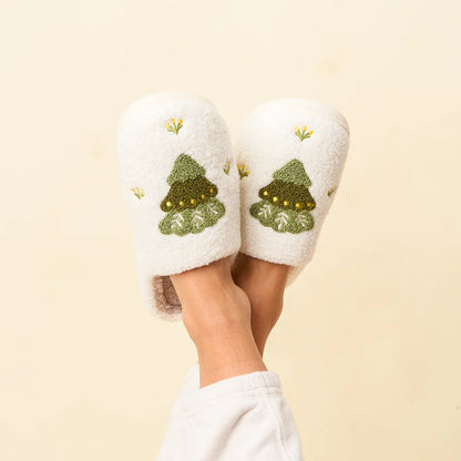 feet crossed in the air wearing white slippers with a tree on each one.