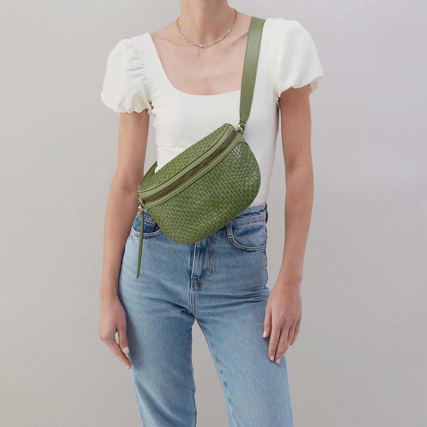 person wearing jeans and a white top with sweet basil juno bag across their chest.