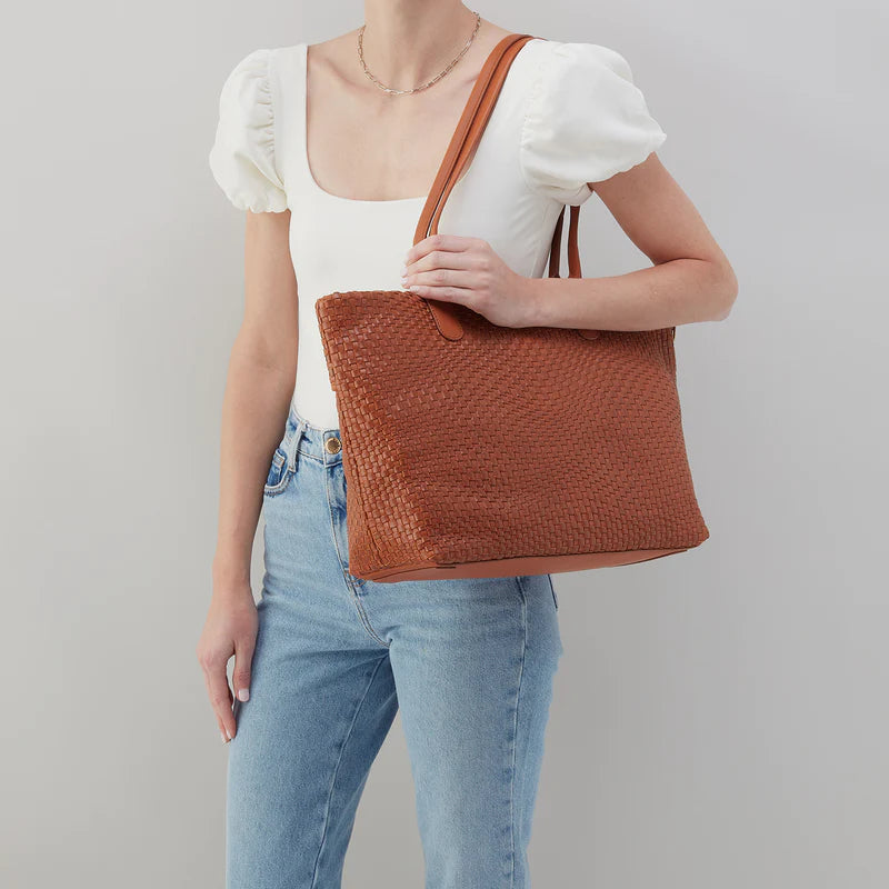 person wearing jeans and a white top with bolder tote on their shoulder.