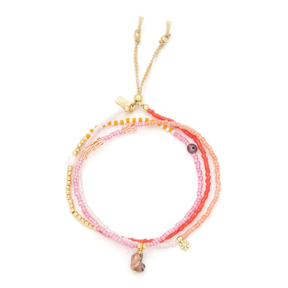 beaded wrap in pink and gold hues shown laying as a triple layered bracelet on a white background
