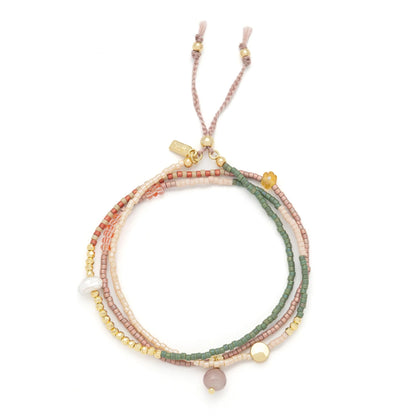 beaded wrap in pink, green, and gold hues shown laying as a triple layered bracelet on a white background
