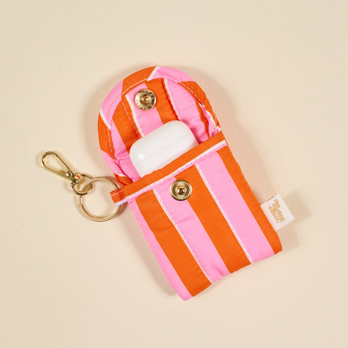 the Puffy Earbud Case in Sicily Stripes Pink with ear buds in it on a beige background