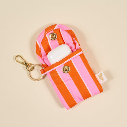 the Puffy Earbud Case in Sicily Stripes Pink with ear buds in it on a beige background