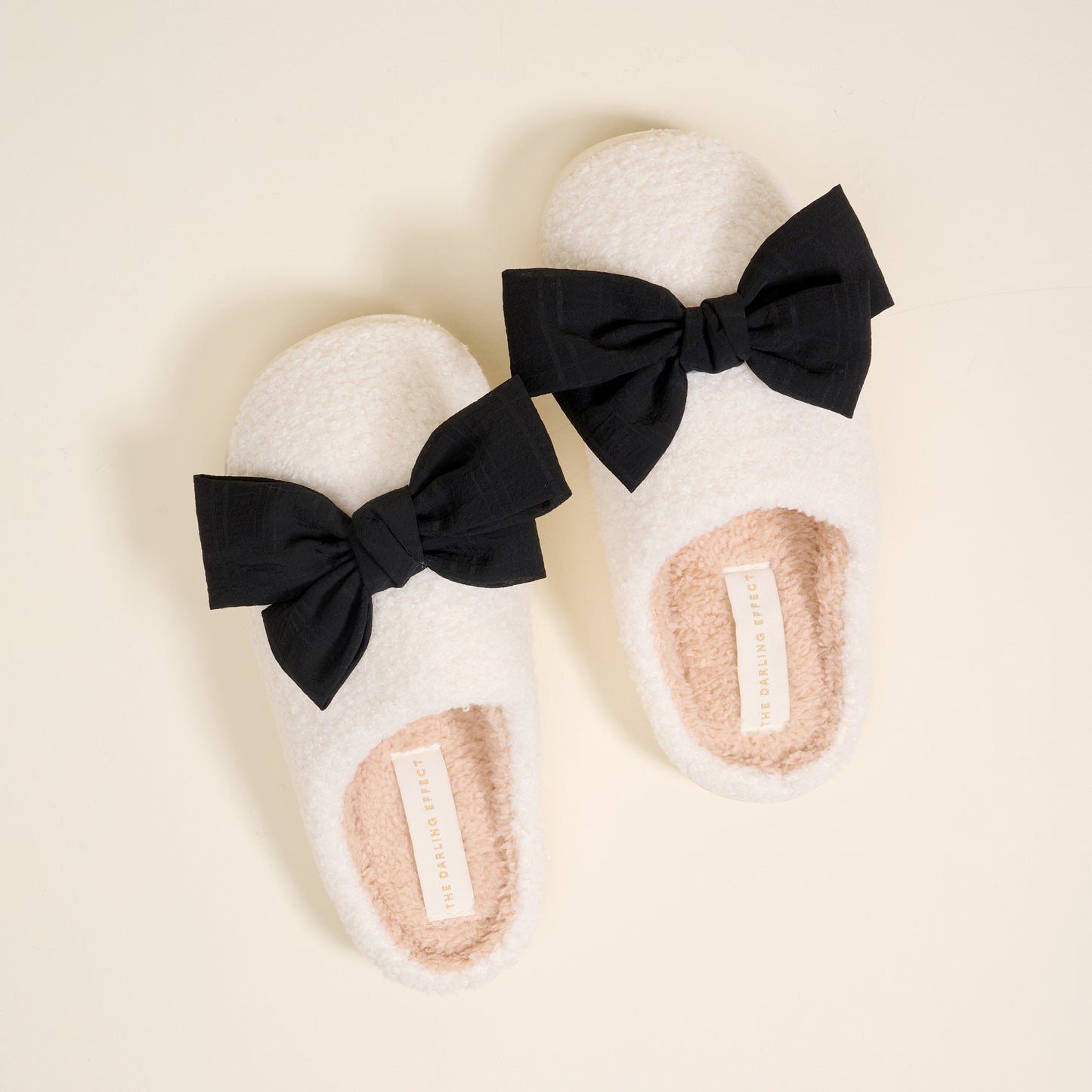 white fuzzy slippers with a black bow on each on a beige background