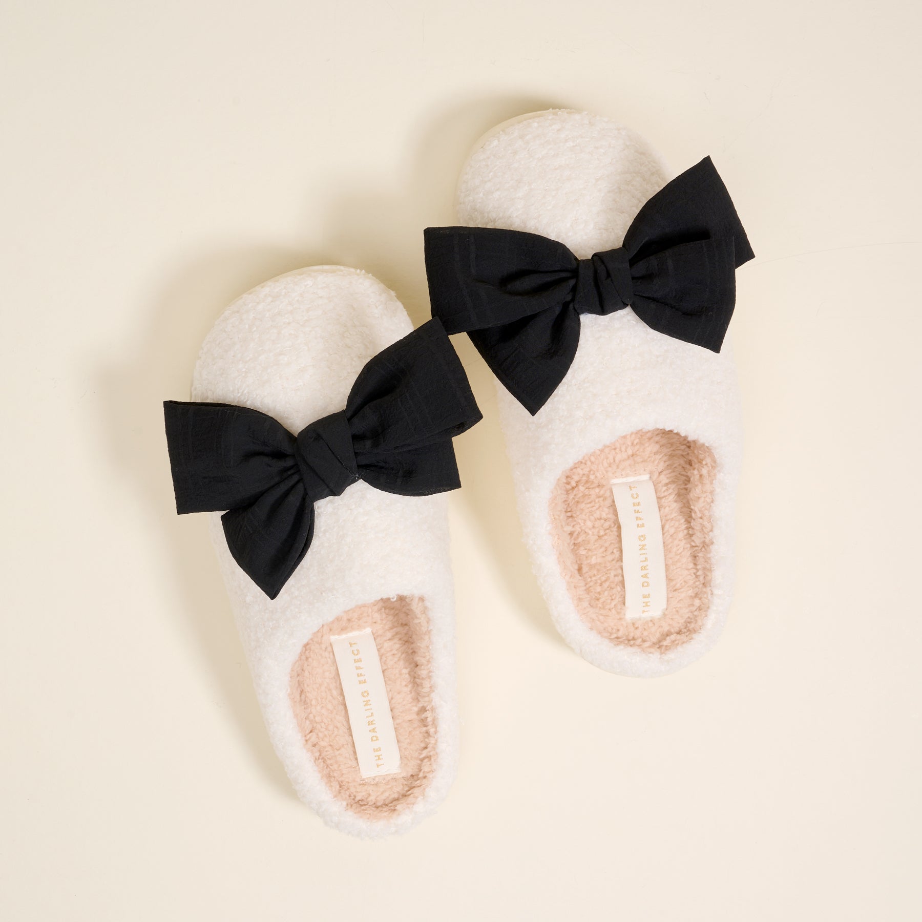 white fuzzy slippers with a black bow on each on a beige background