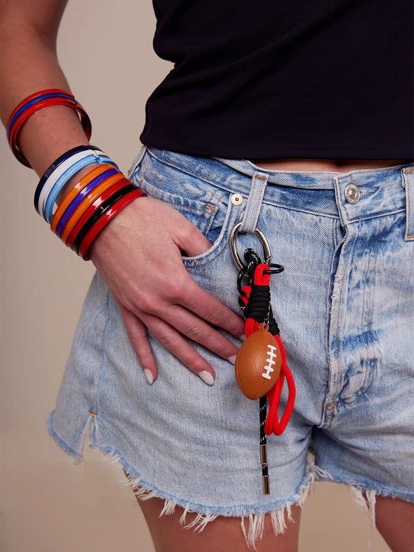 person wearing jean shorts with red football bag charm clipped on belt loop