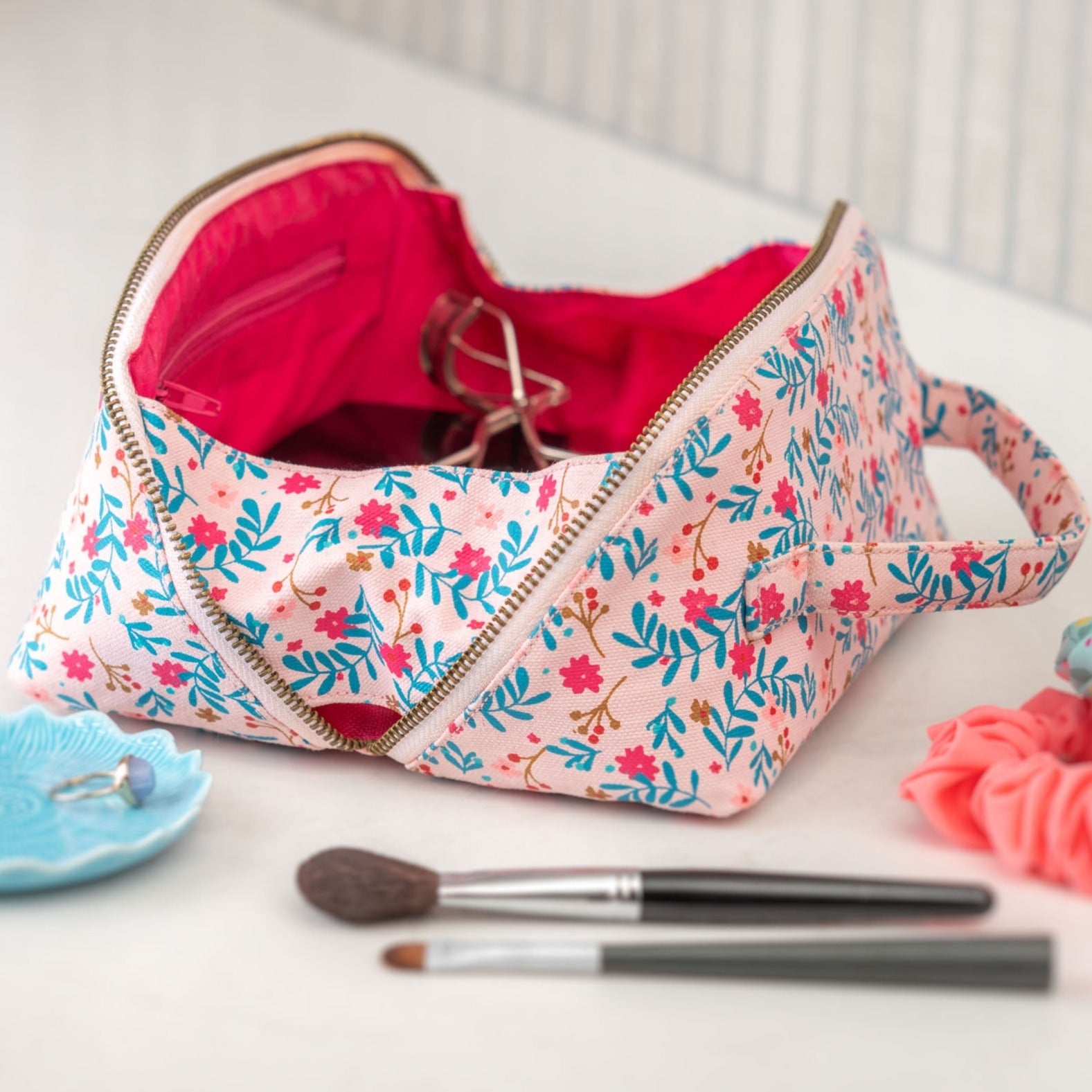 blush floral zip bag open on a counter with cosmetics inside and out.