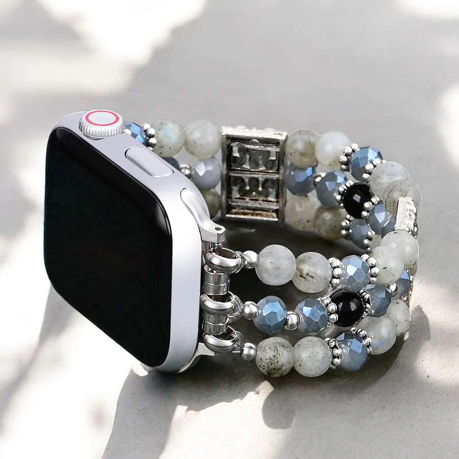 Smartwatch with a beaded strap with white, blue, black, and silver beads on a light background