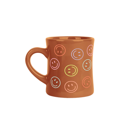 A terracotta brown ceramic mug decorated with a pattern of colorful smiley faces in various outlines, shown against a plain white background.