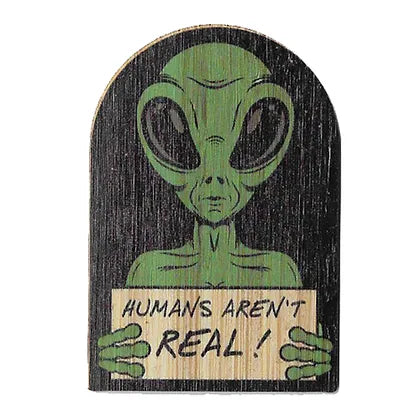 green alien on a black background holding a sign that says "humans aren't real!"