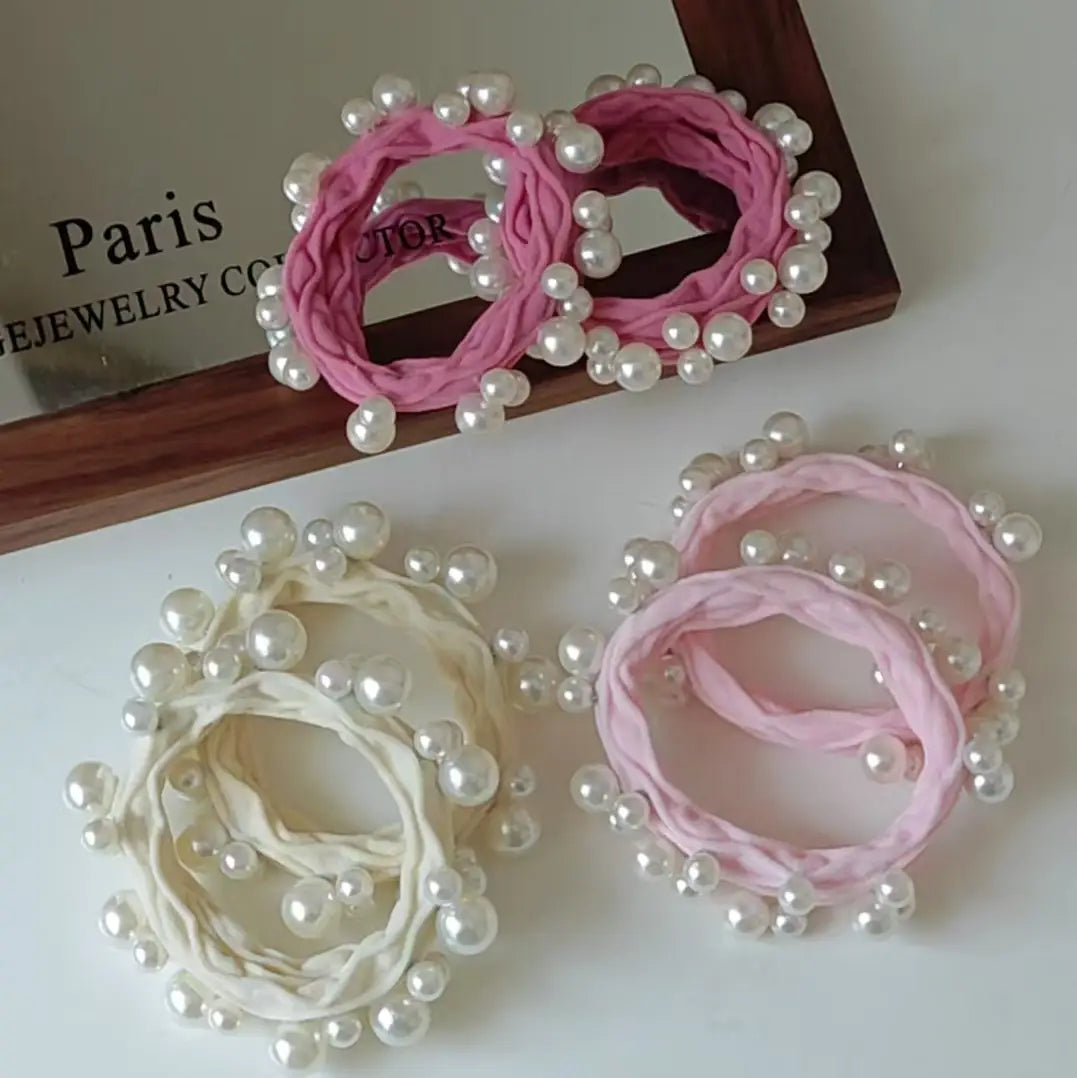 6 hair ties in cream and 2 shades of pink  with pearls sewed on them arranged on a white surface