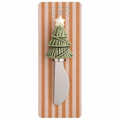 A decorative spreader with a Christmas tree handle, featuring a green tree with a white star topper, mounted on a striped cardboard backing.