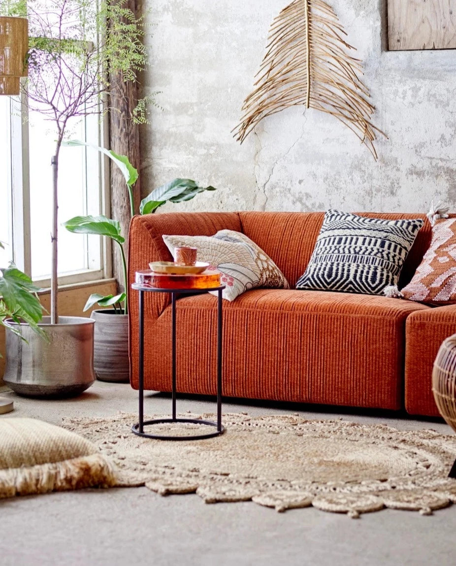 assorted pillows on an orange couch with plants and a coffee table near by.