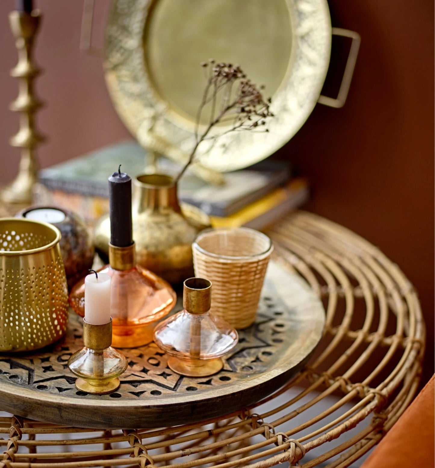three glass and metal taper holders displayed on a metal tray next to brass vases, candles, and votive holders